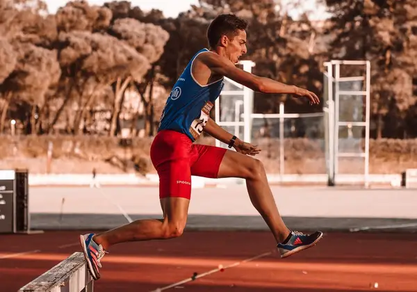 A track athlete clearing a hurdle in full stride