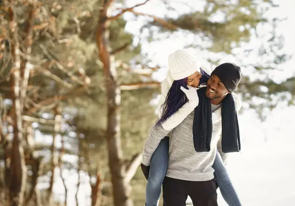 A husband giving his wife a piggyback ride on a winter walk