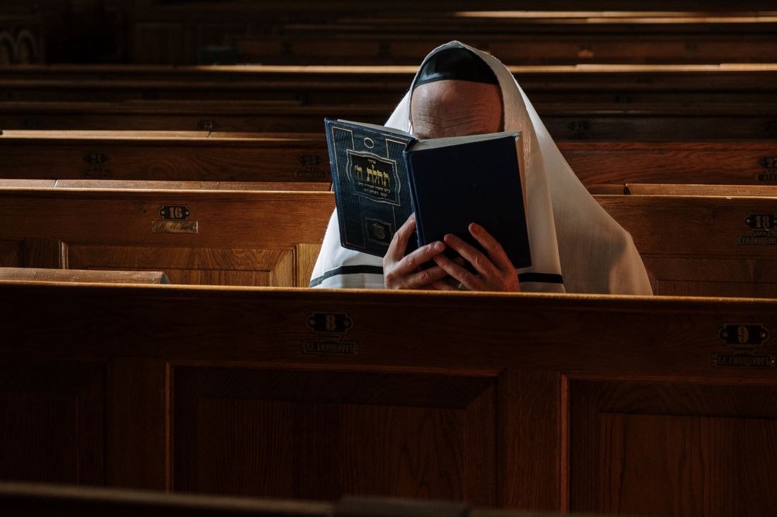 A man wrapped in a prayer shawl reading from the prayer book
