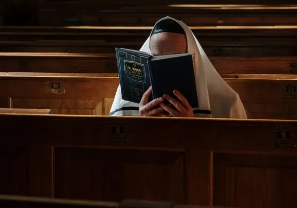 A man wrapped in a prayer shawl reading from the prayer book