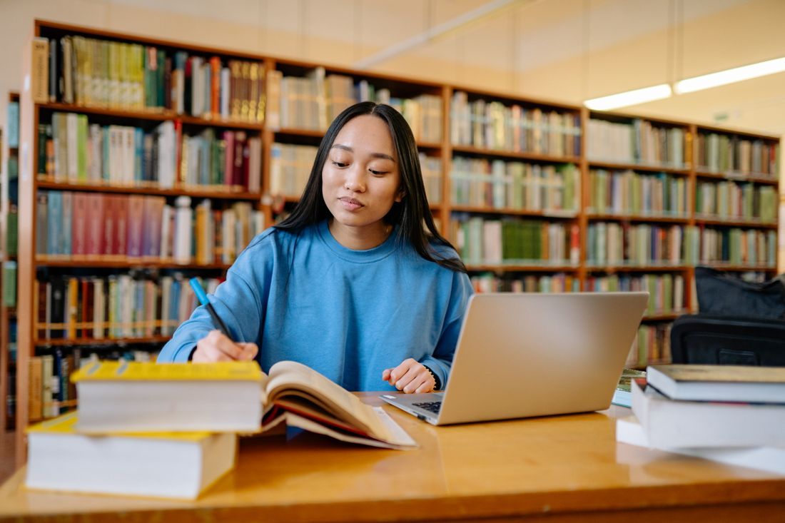A college student studying with a laptop and books in the library