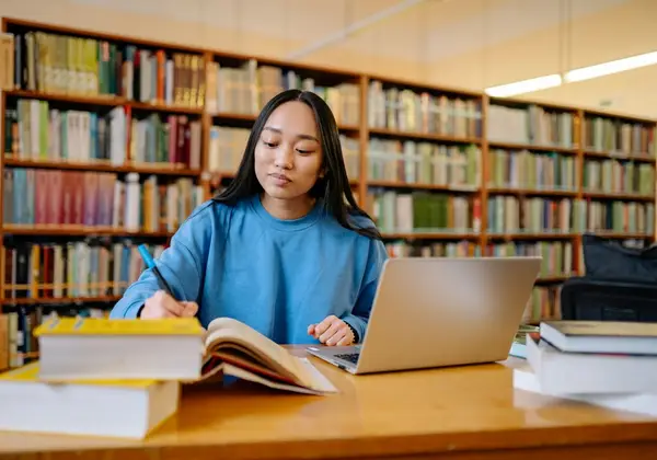 A college student studying with a laptop and books in the library
