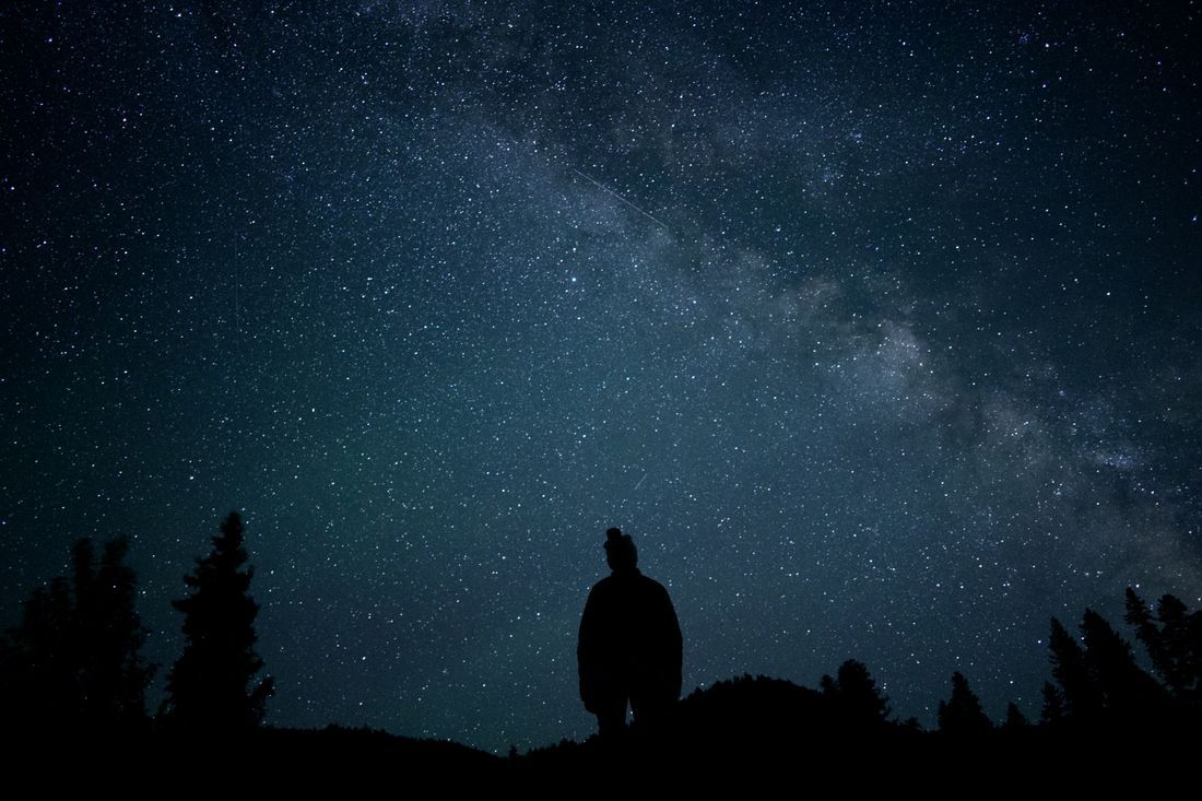 A figure silhouetted under the Milky Way, wondering