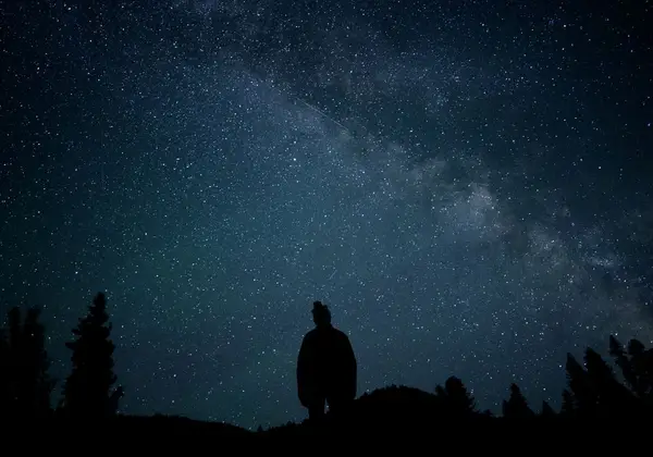 A figure silhouetted under the Milky Way, wondering