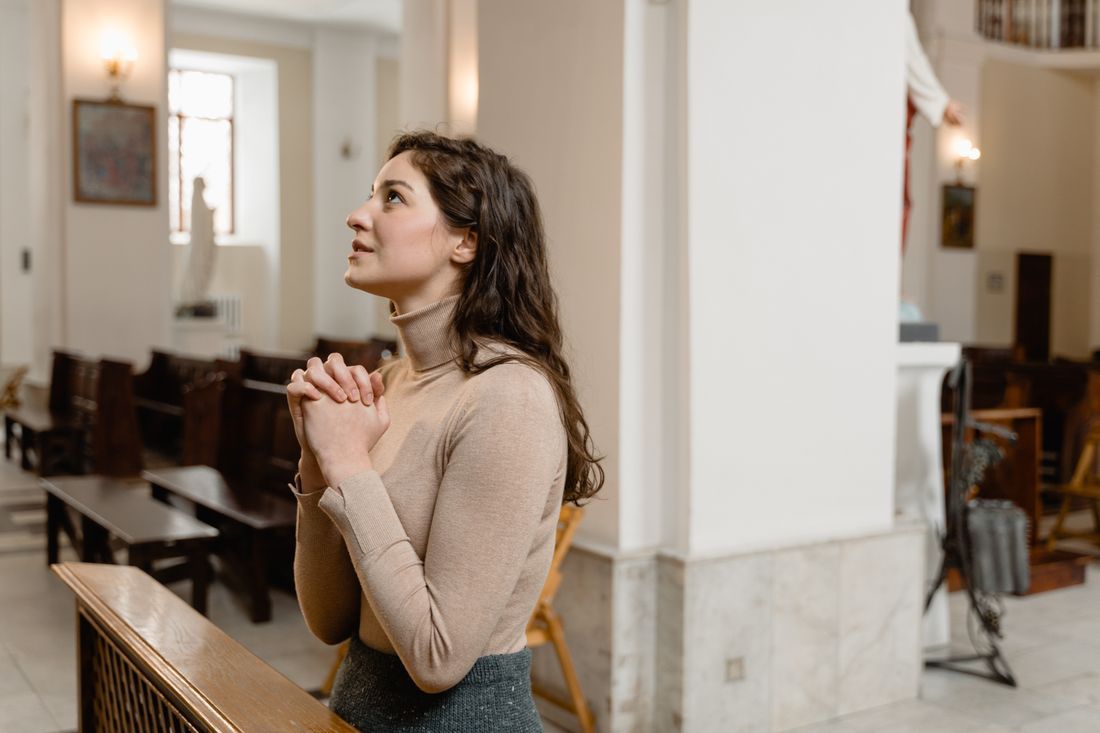 A woman kneeling in prayer, looking up with hope