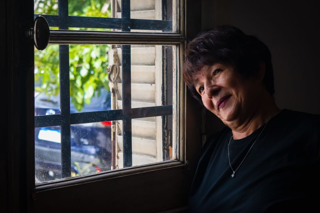 An older woman by a window with a gentle, hopeful expression