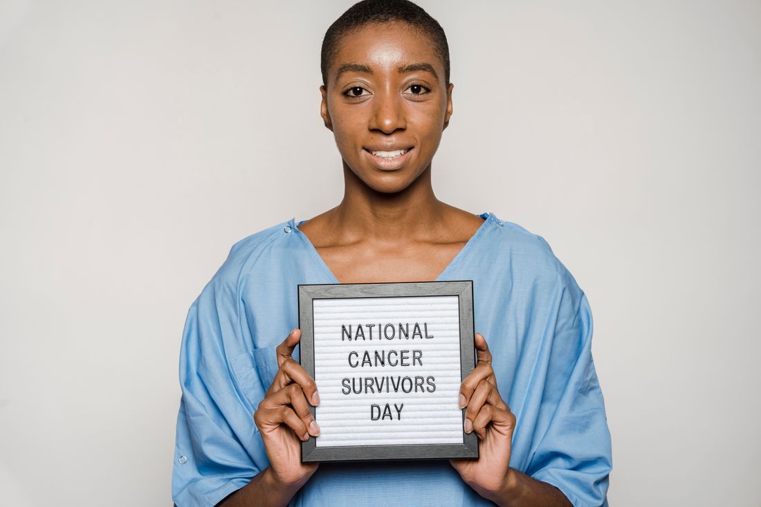 A smiling woman holding a National Cancer Survivors Day sign