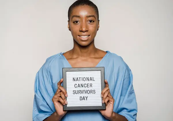 A smiling woman holding a National Cancer Survivors Day sign