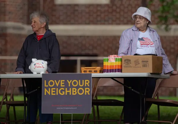 Two faithful volunteers serving at a church 'love your neighbor' table