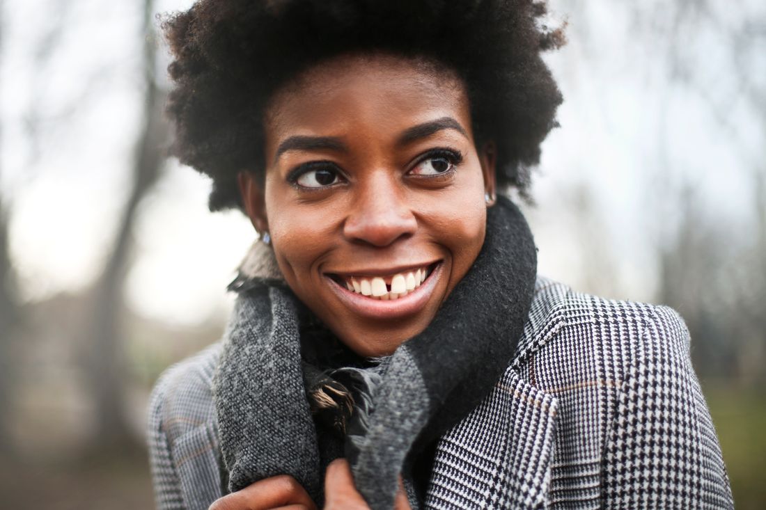 A woman smiling warmly outdoors in a scarf