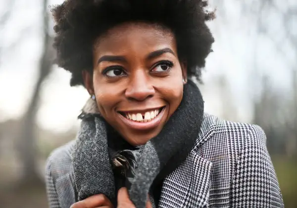 A woman smiling warmly outdoors in a scarf