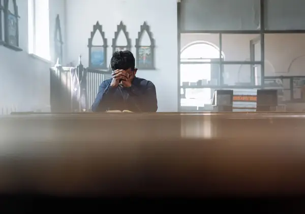 A young man with his head resting on clasped hands in prayer