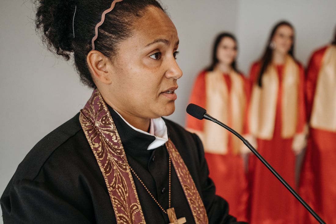 A woman pastor speaking, with a choir behind her