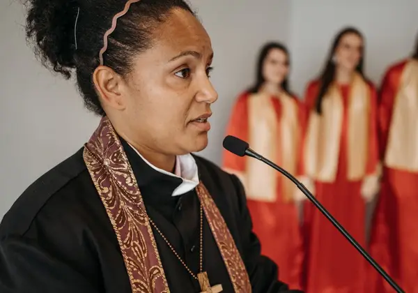 A woman pastor speaking, with a choir behind her