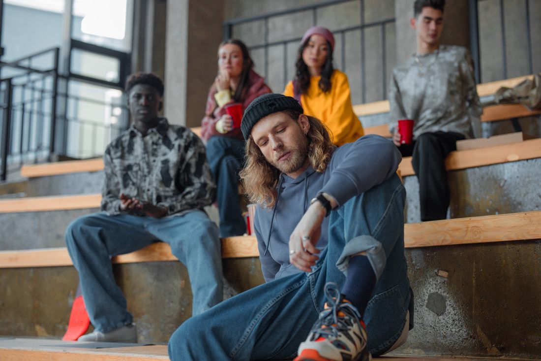 A young man sitting apart on bleachers, weighed down, while others talk