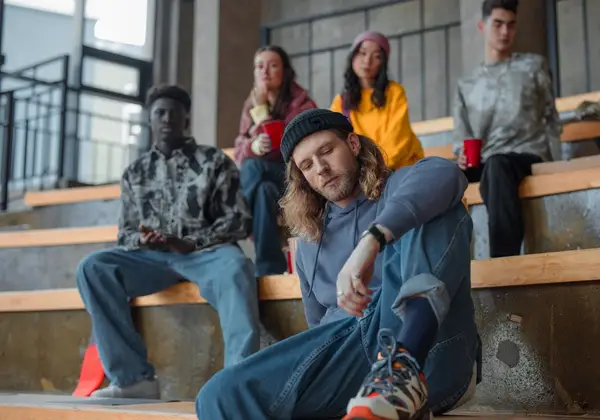 A young man sitting apart on bleachers, weighed down, while others talk