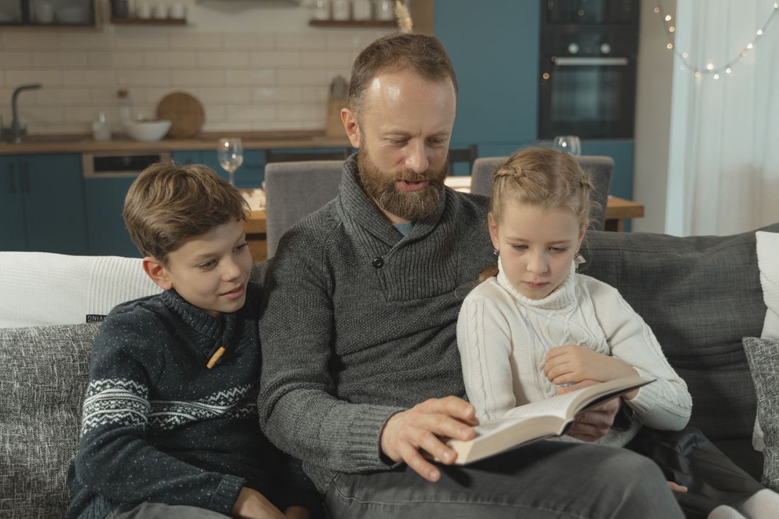 A father reading a book with his son and daughter on the couch