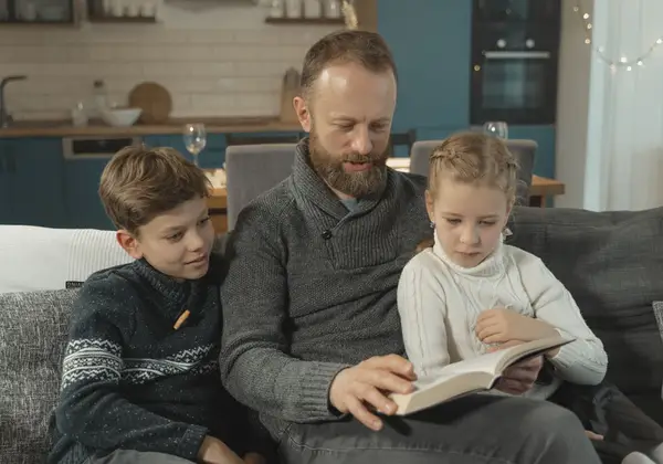 A father reading a book with his son and daughter on the couch