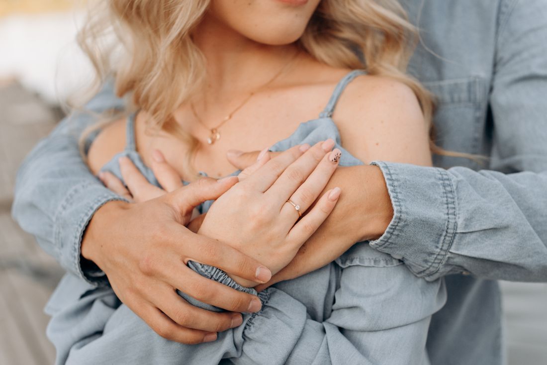 A husband embracing his wife from behind, hands clasped over her heart