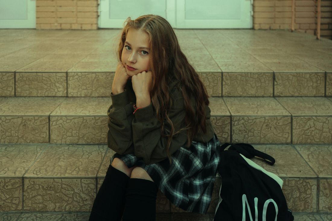 A teenage girl sitting on steps, chin resting on her hands, thoughtful