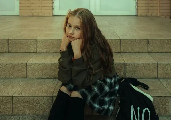 A teenage girl sitting on steps, chin resting on her hands, thoughtful