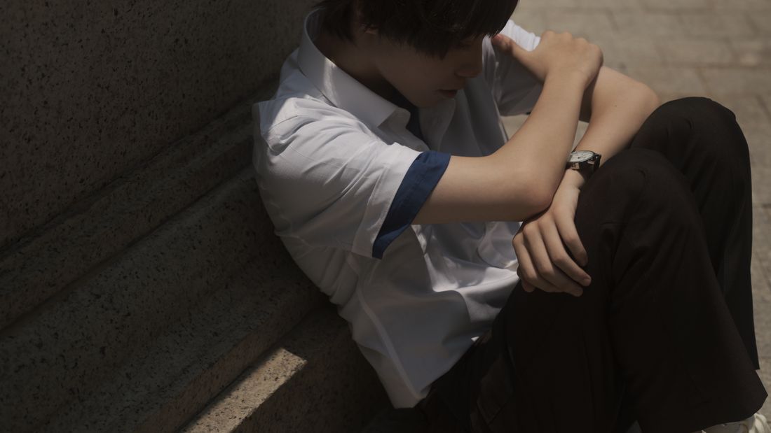A teenage boy sitting alone on steps, head down under the weight