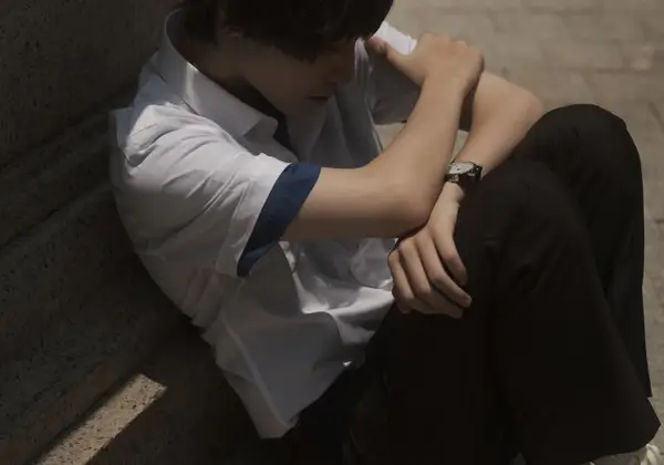 A teenage boy sitting alone on steps, head down under the weight