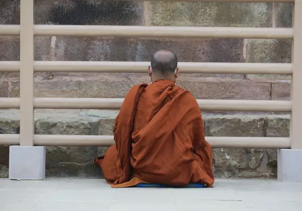 A monk seated in meditation before a temple wall