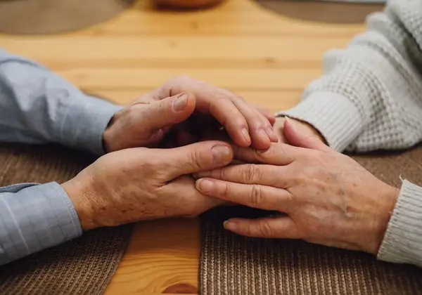 Two pairs of weathered hands joined across a table
