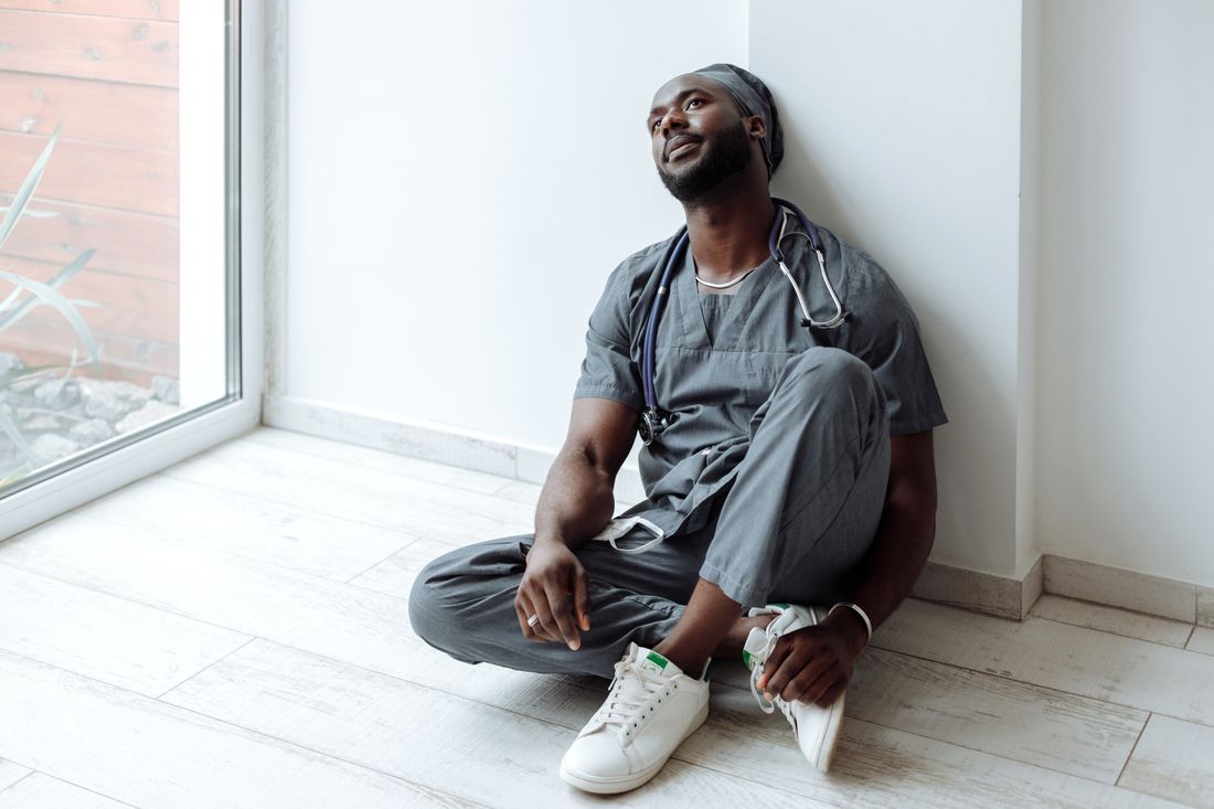 A nurse sitting against a wall, taking a weary moment to breathe