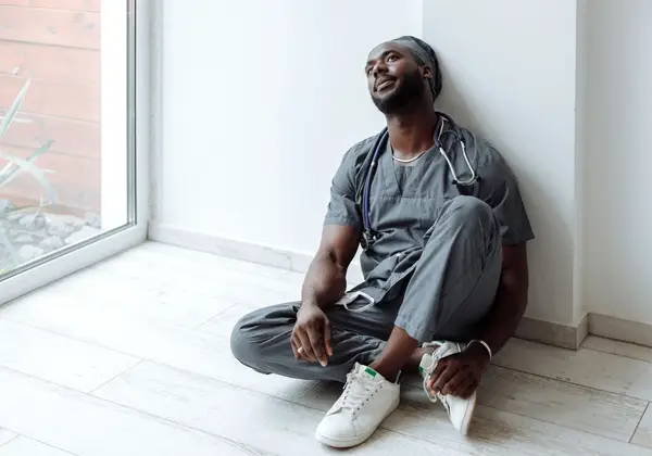 A nurse sitting against a wall, taking a weary moment to breathe