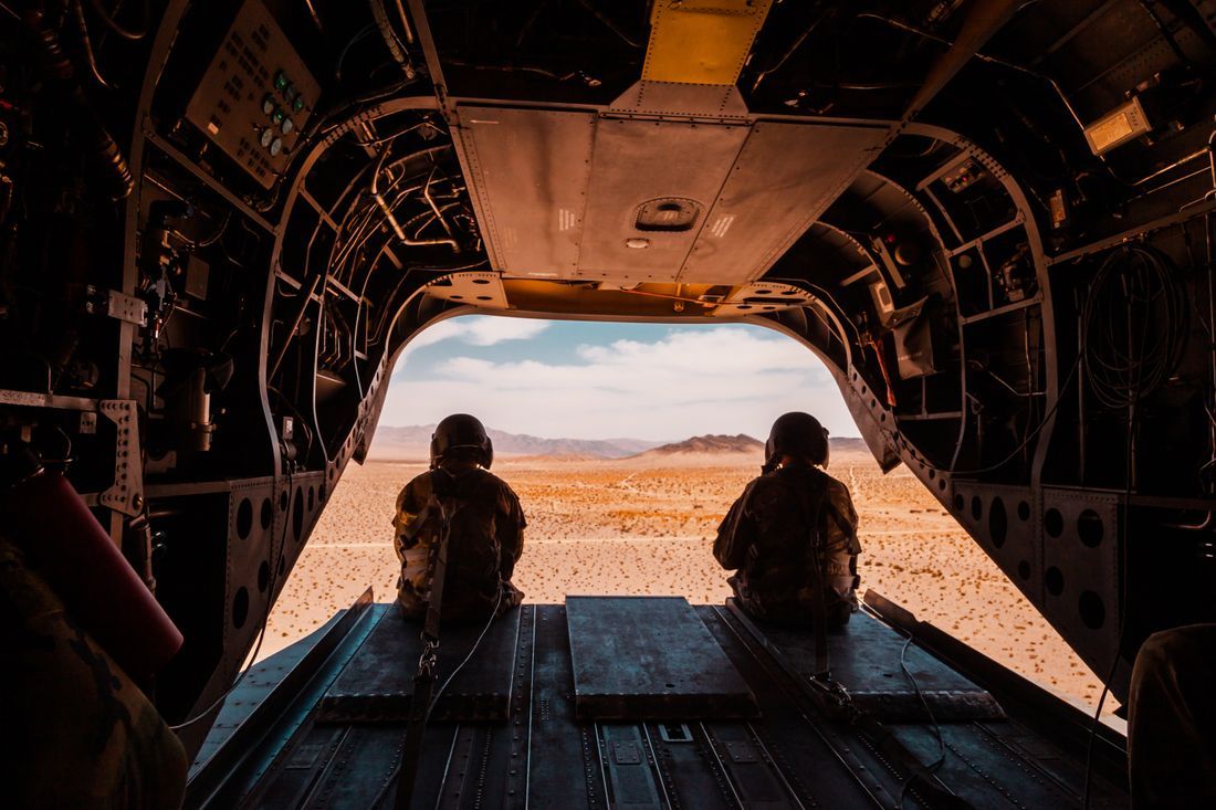 Two service members seated at the open ramp of a helicopter over the desert