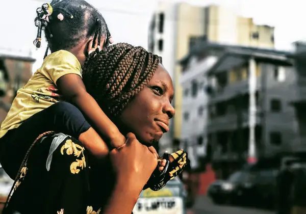 A mother carrying her daughter on her shoulders through the city