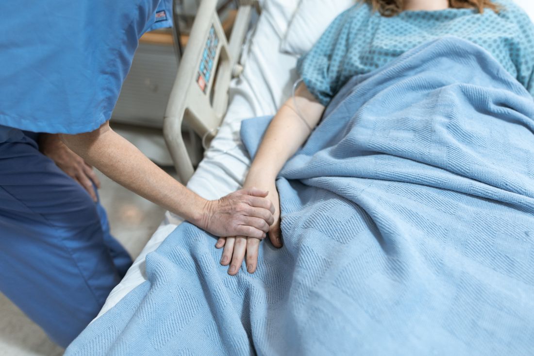 A nurse gently holding a patient's hand at the bedside