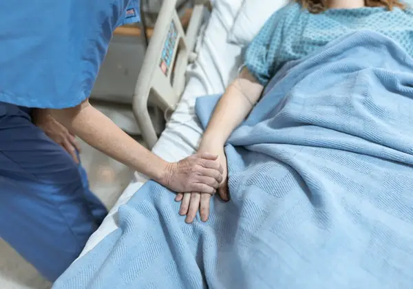 A nurse gently holding a patient's hand at the bedside