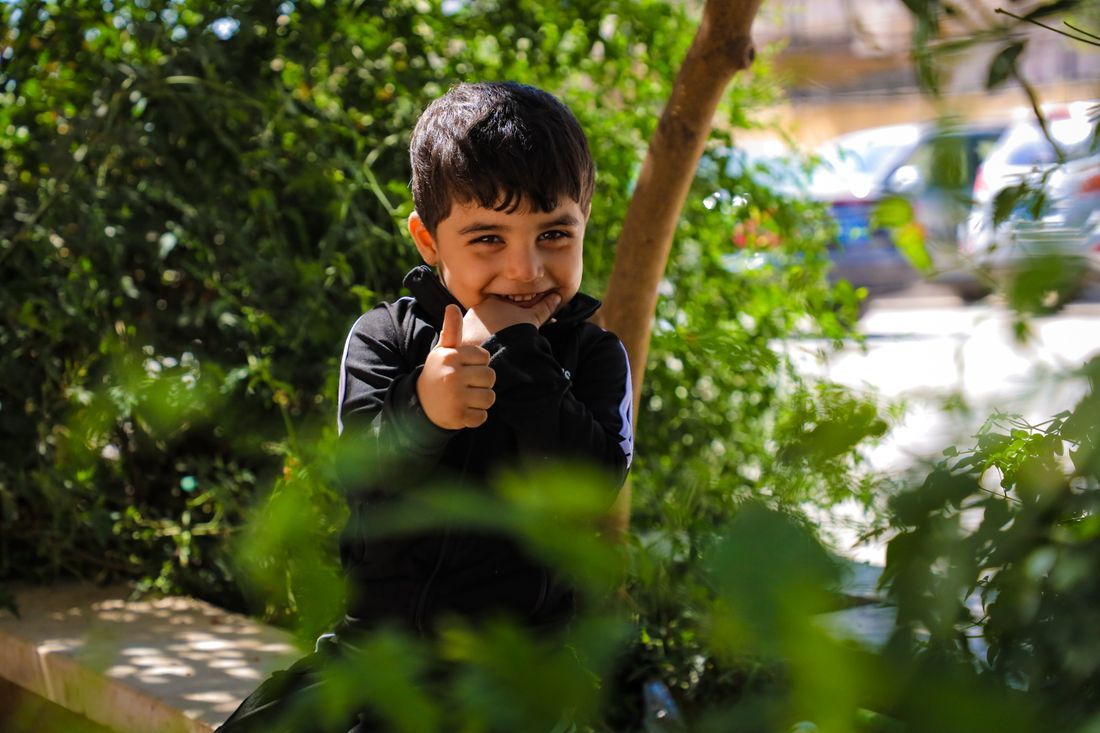 A smiling boy giving a thumbs up outdoors