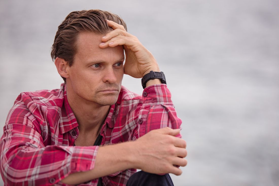 A man sitting alone by the water, weighed down in thought