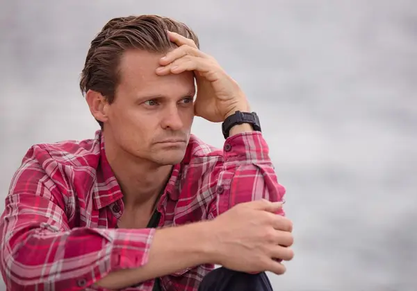 A man sitting alone by the water, weighed down in thought