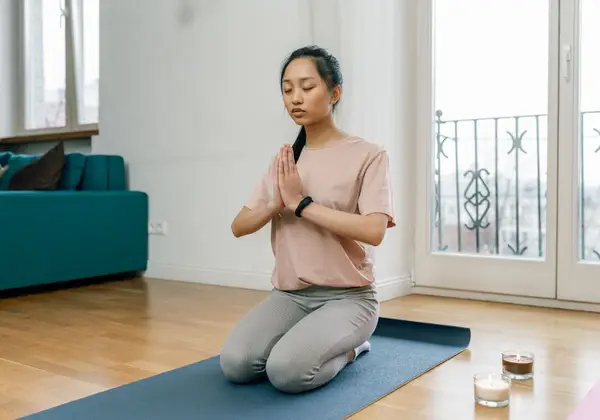 A woman meditating peacefully at home by a sunlit window