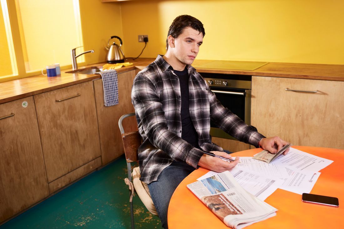 A young man sitting with paperwork at the kitchen table