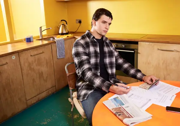 A young man sitting with paperwork at the kitchen table