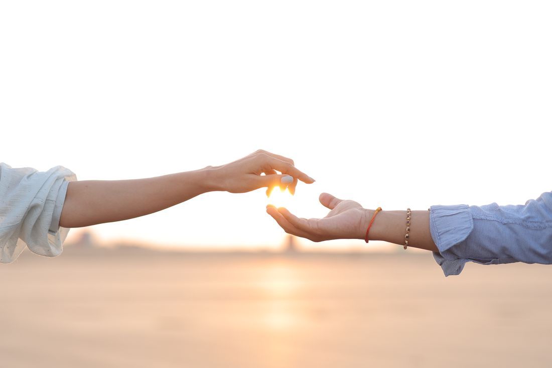 Two hands reaching toward each other with the sun between them