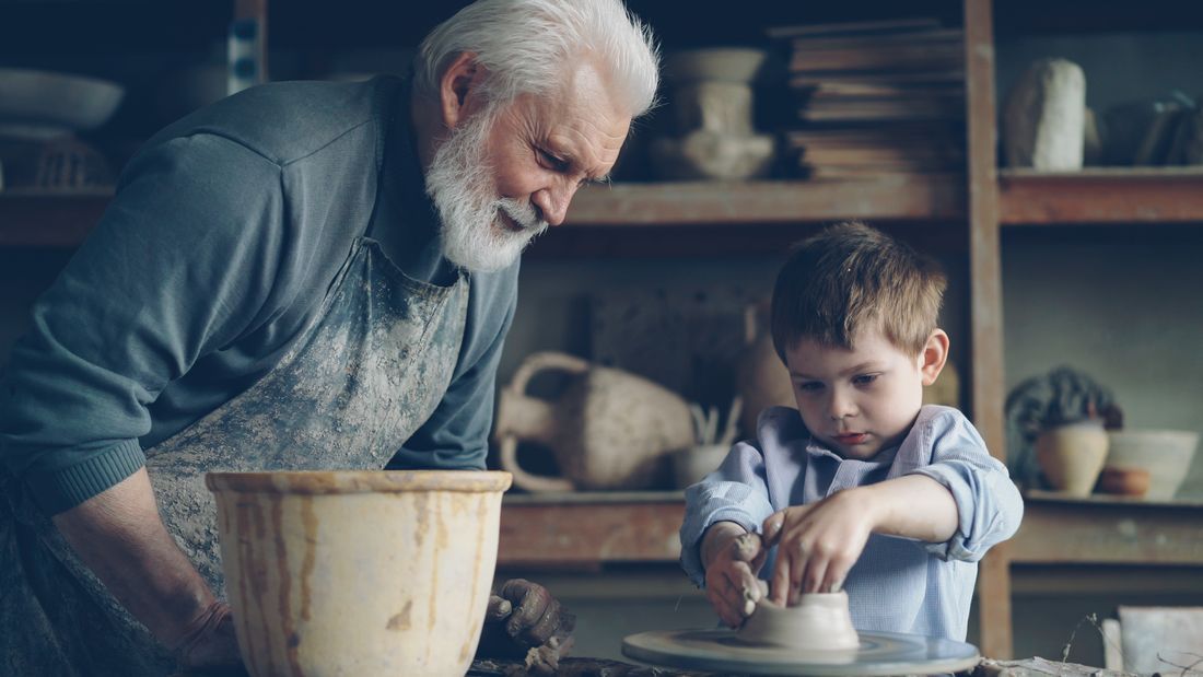 A grandfather teaching his grandson at a pottery wheel