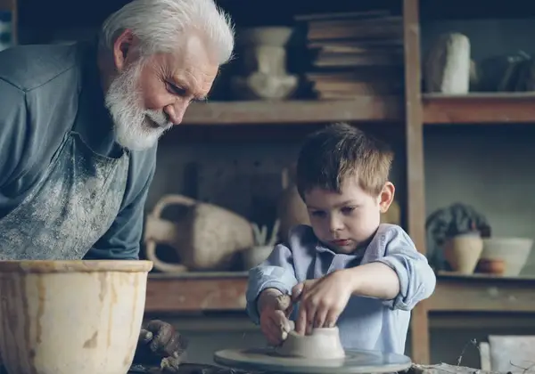 A grandfather teaching his grandson at a pottery wheel