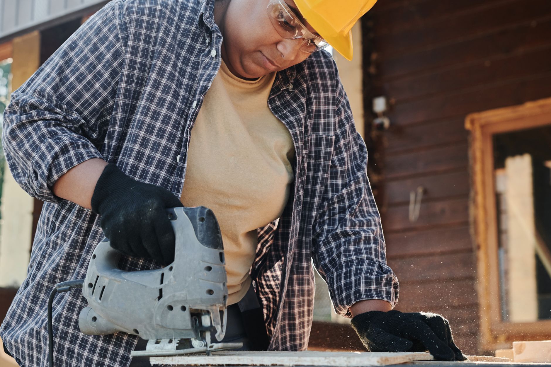 A woman in a hard hat focused on cutting wood on a build site