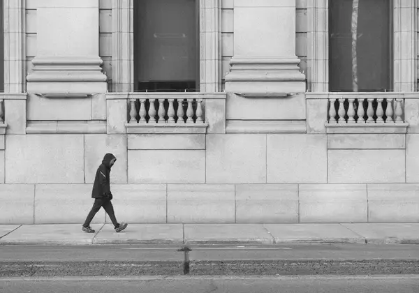 A lone figure walking past a grand stone building
