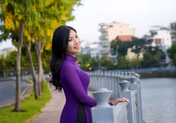 A Vietnamese woman in a purple ao dai by the river