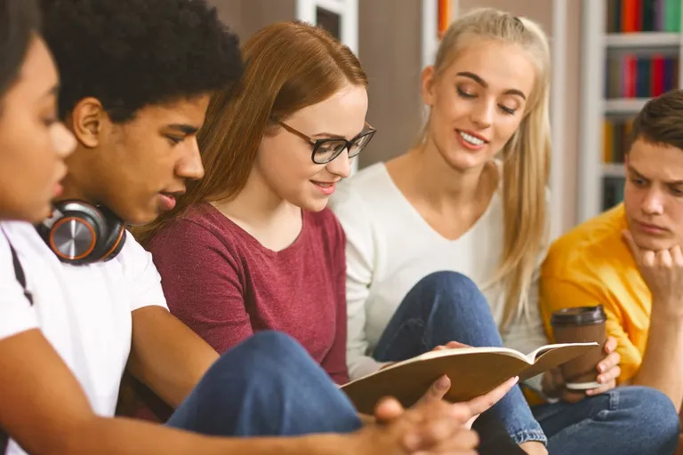 People studying together over open books in a library — the posture of seeking the wisdom our Father gives freely to everyone who asks.
