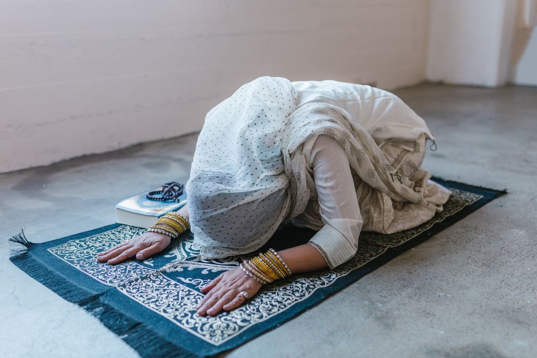 A woman in prayer on a mat with prayer beads beside her