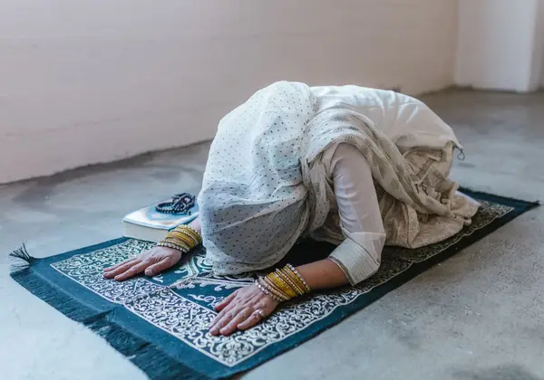 A woman in prayer on a mat with prayer beads beside her